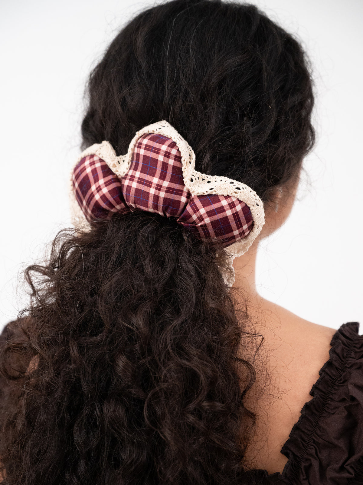 The silk Wildpetal holding curly hair half-up, seen from behind: maroon plaid petals edged in cream lace