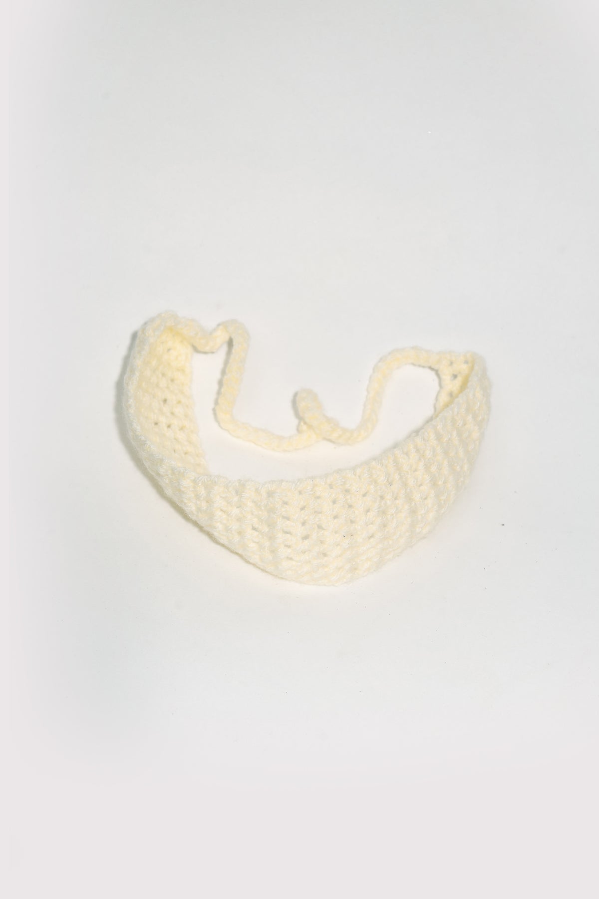 The ivory crochet headband curved into a horseshoe, ties crossing at the centre, on a soft white ground