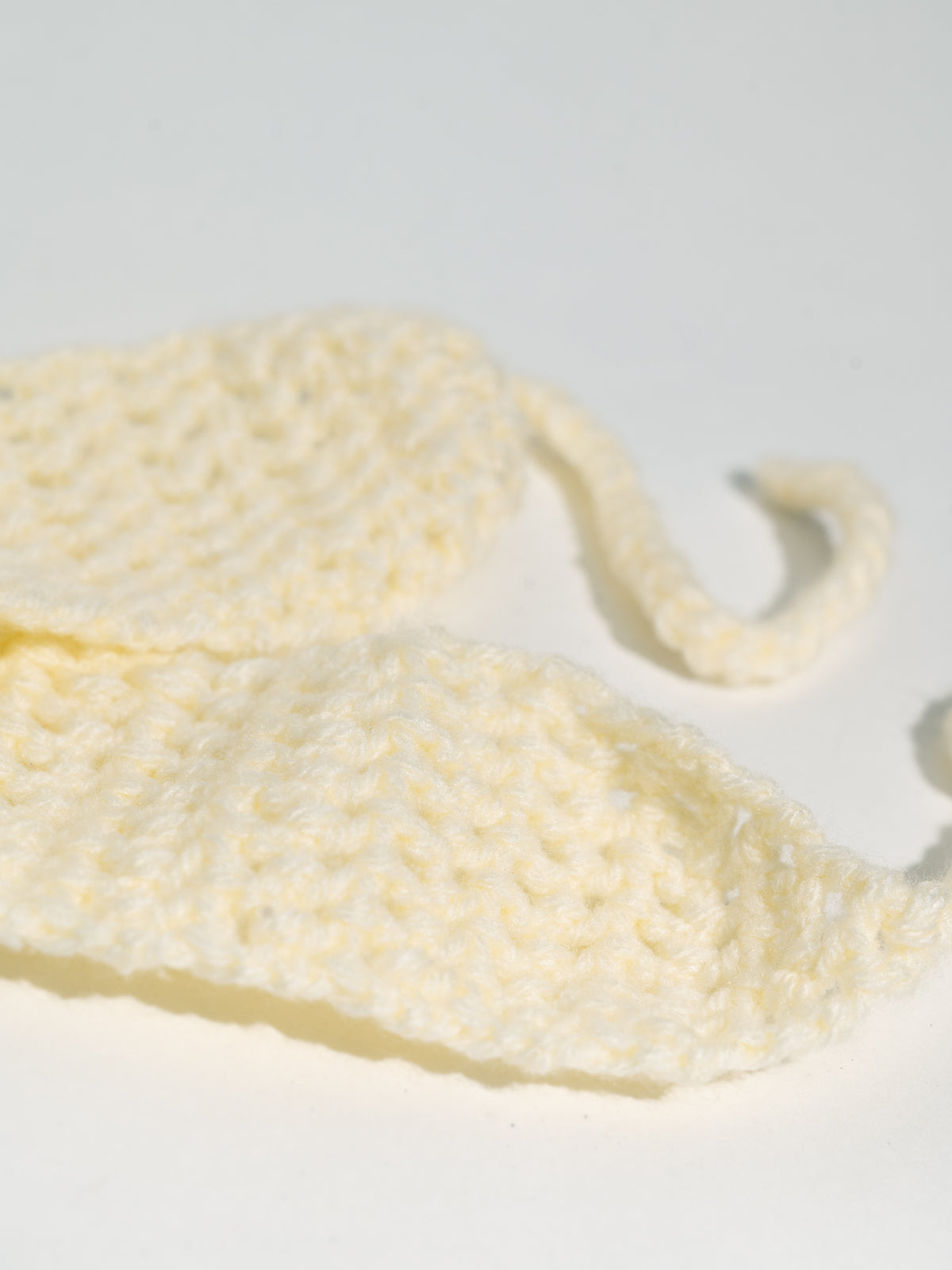 Close-up of Mellow's crochet: open cream loops and the ties worked straight from the band's ends