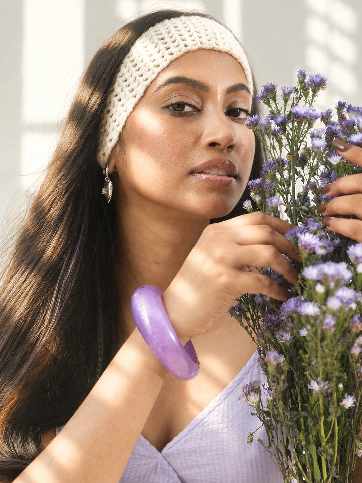 The ivory headband sitting low and soft, a lilac bangle on the wrist, flowers in hand