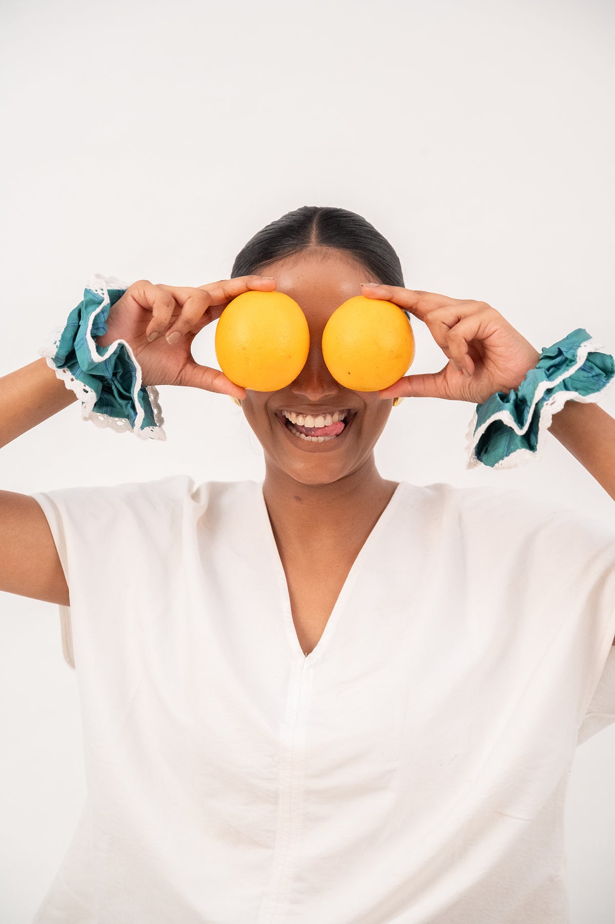 Two oranges held up as eyes and a wide smile, a Rainfern scrunchie on each wrist