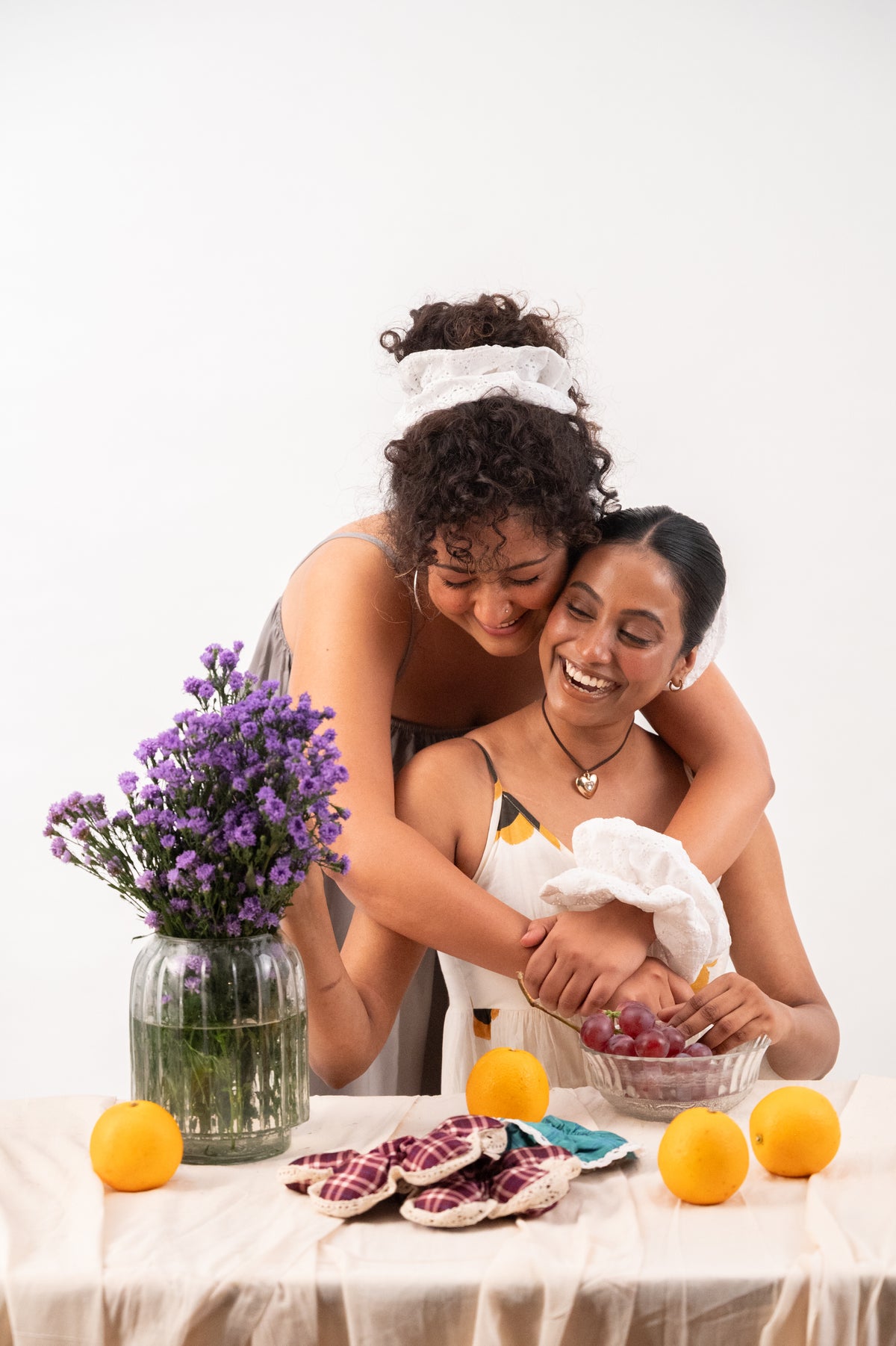 Two friends hugging beside a jar of purple flowers, Cloudy tied in one's hair