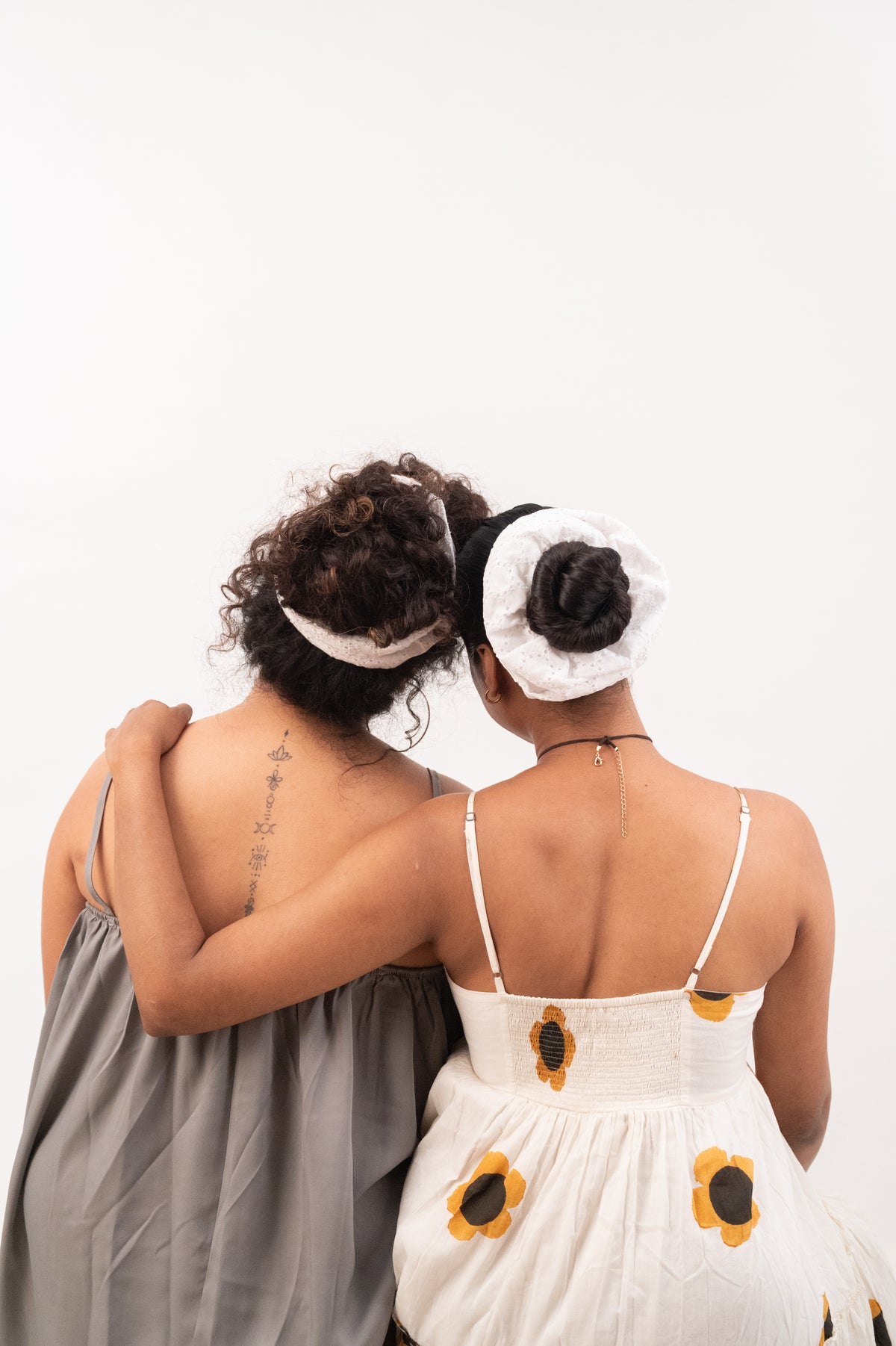 Two friends from behind, arms around each other, their buns tied with Cloudy