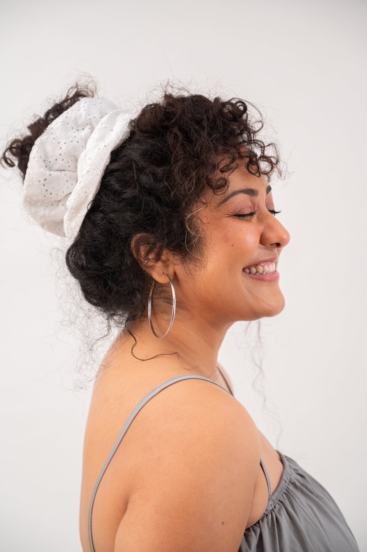 Curly hair piled into a bun with Cloudy, the white chikankari scrunchie, and a wide smile