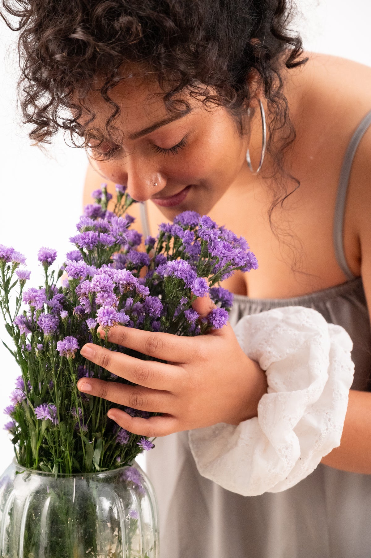 Cloudy, the white chikankari scrunchie, on a wrist while she breathes in a bunch of purple flowers