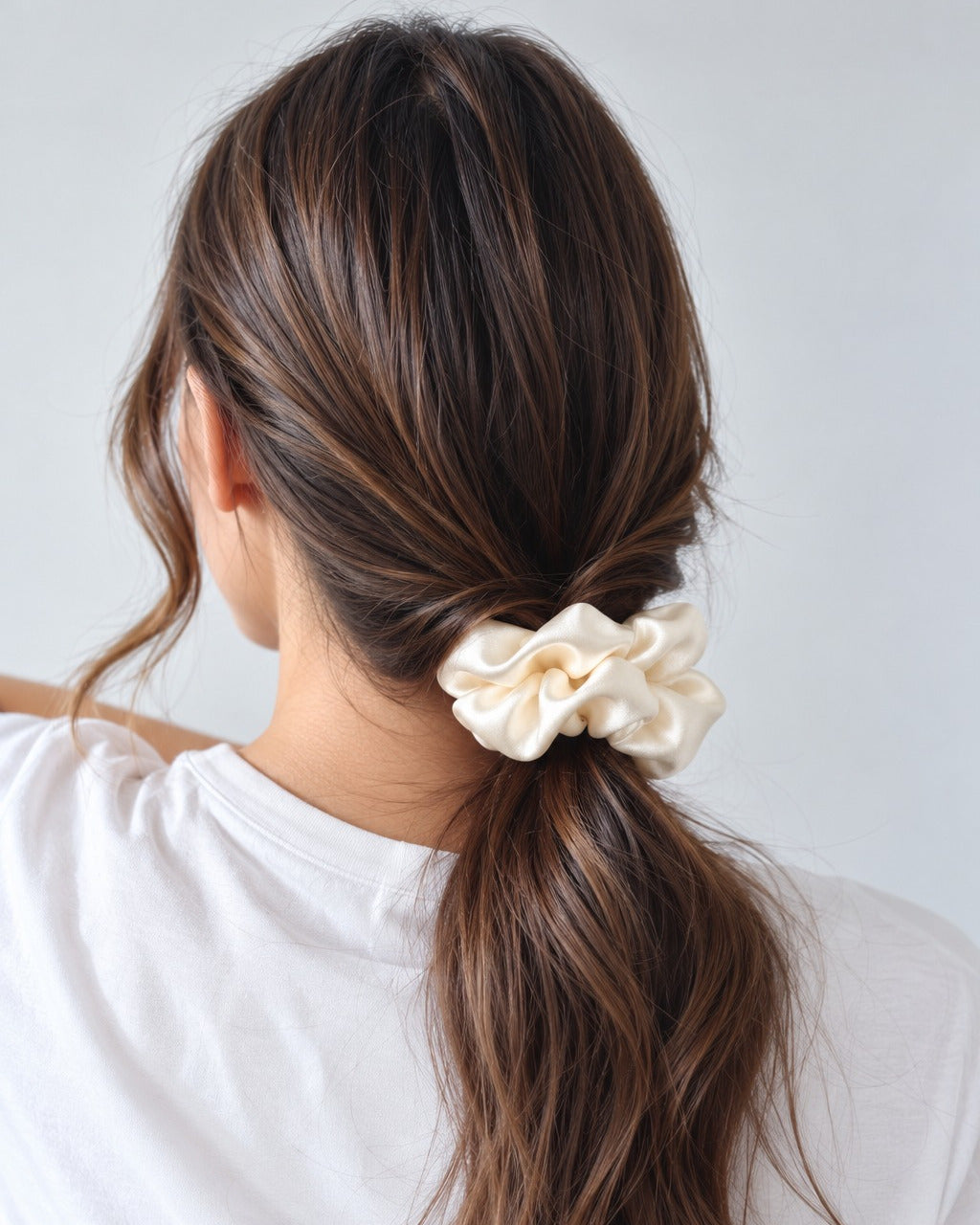 Candy Pop mulberry silk charmeuse scrunchie in Antique White, holding a low ponytail