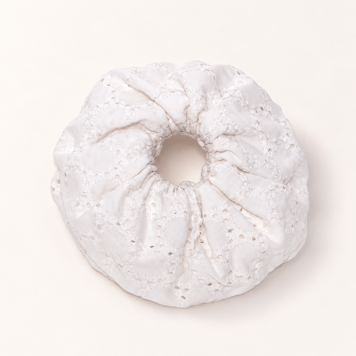 Cloudy white eyelet-embroidered scrunchie on a warm ivory studio background