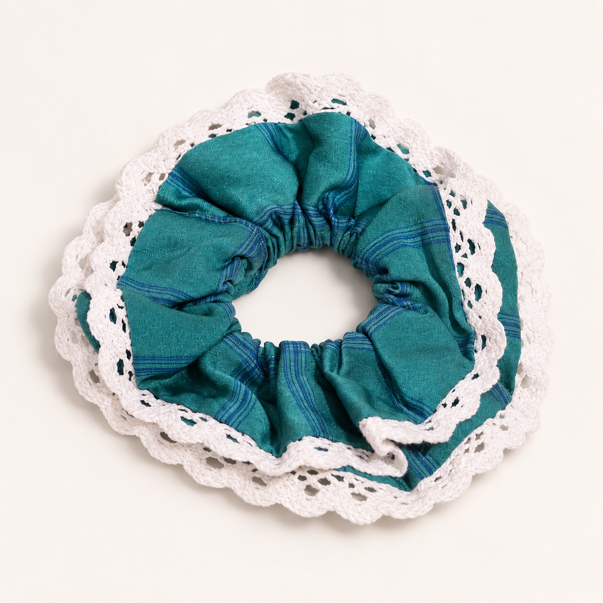 Rainfern teal striped scrunchie with white scalloped lace trim on a warm ivory studio background