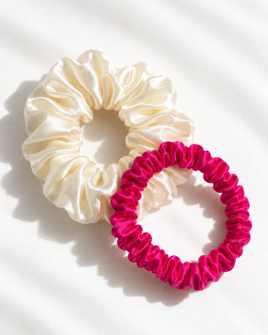 Size comparison: thin Candy Dot silk scrunchie in Hot Pink beside a big Candy Pop in Antique White