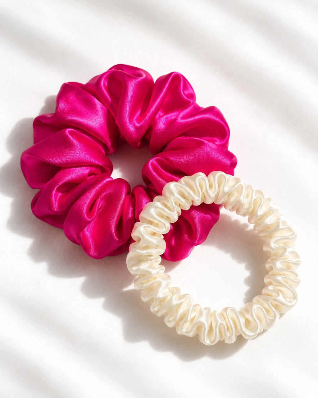 Size comparison: thin Candy Dot silk scrunchie in Antique White beside a big Candy Pop in Hot Pink