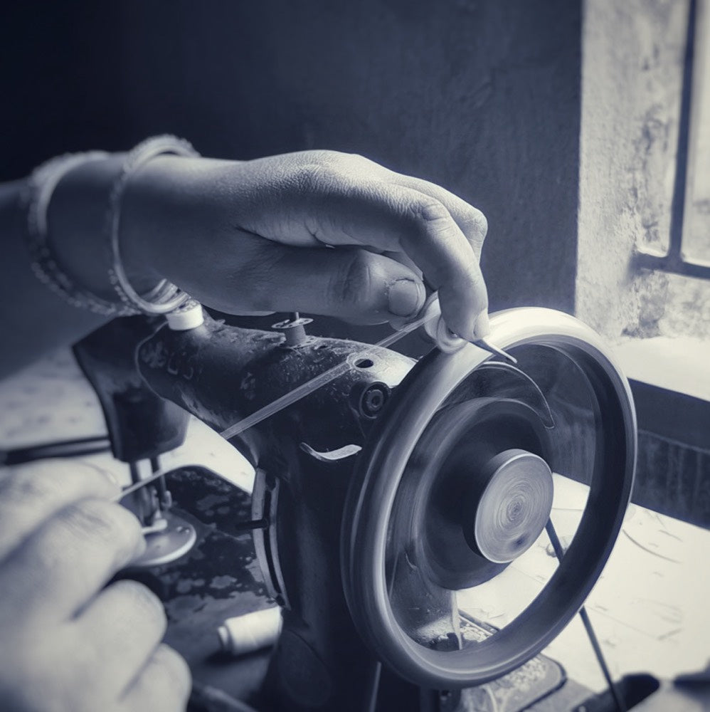A hand turning the wheel of an old sewing machine by a window